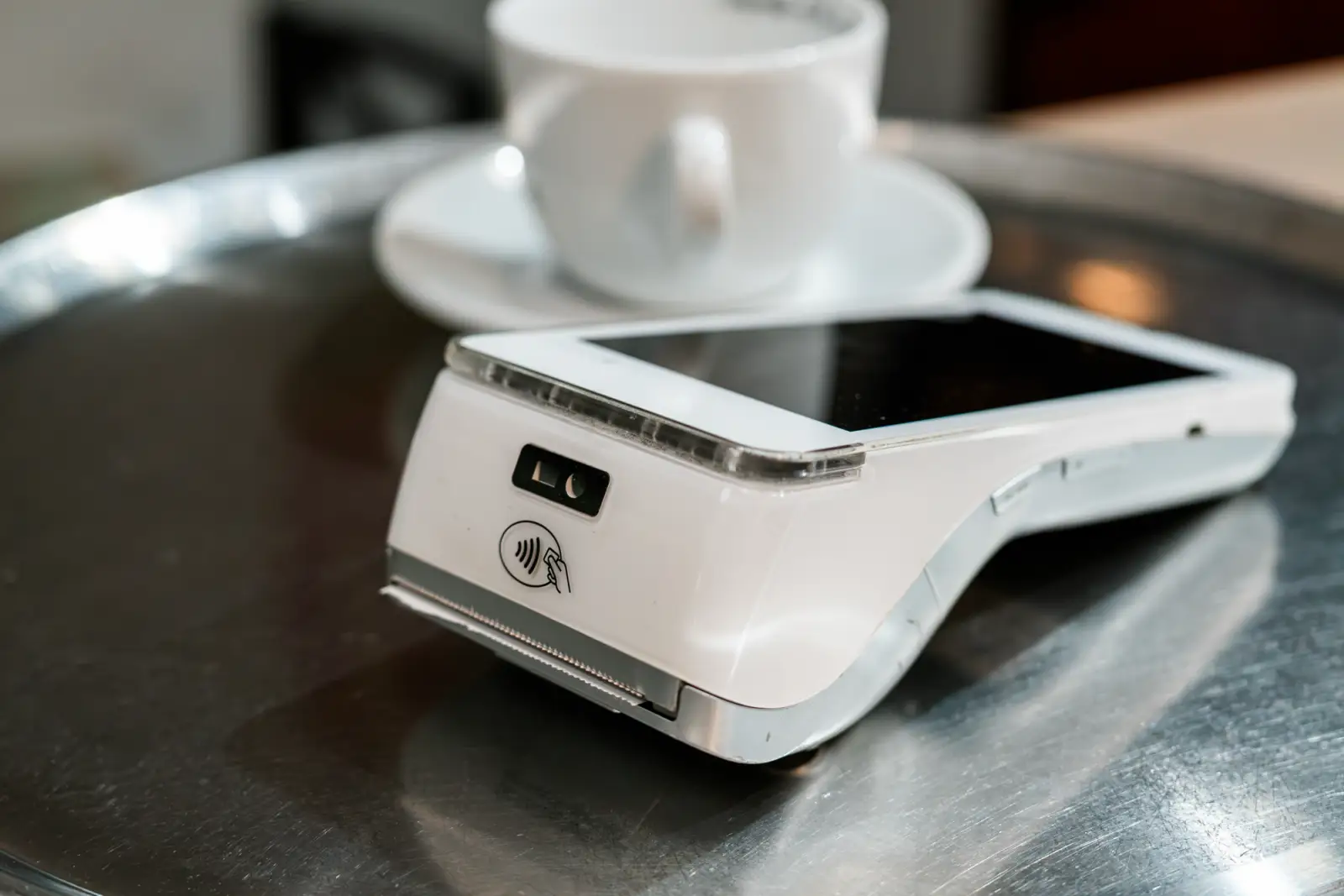 A portable card terminal on a café tray beside a coffee cup